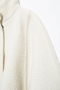 Detailed close-up of thick white textured boucle fabric and stitching on the cape coat