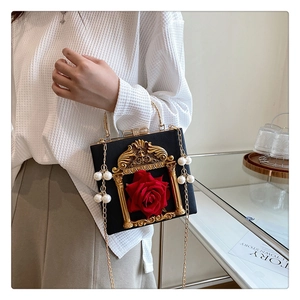 Detail of vintage black handbag with golden frame, red rose, and pearl tassels detail