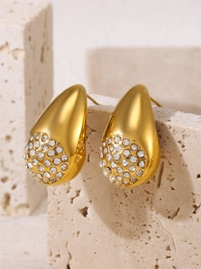 Detail of teardrop earrings with gold plating and paved white zircons on beige stone