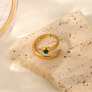 Macro view of a 18K gold plated snake ring with green stone eye on beige stone