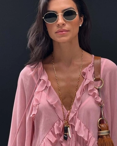 Détail de robe rose à volants col V avec collier long doré et sac à main en cuir