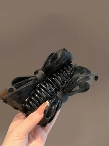 Close-up of elegant black polka dot organza bow hair claw clip held in hand