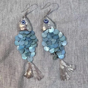 Macro detail of fish-shaped earrings with blue shell scales and evil eye design