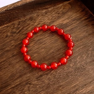 Close-up of red agate beaded bracelet on a vintage dark wood tray showing glossy details