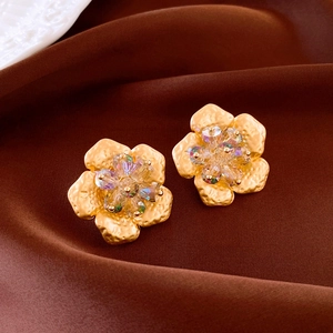Macro shot of gold metal flower earrings with crystal centers on brown satin fabric