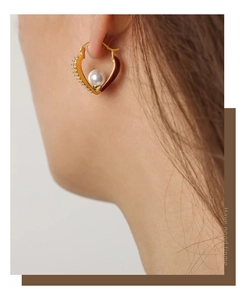Close-up of heart-shaped gold earring with pearl, crystals and deep red enamel detail