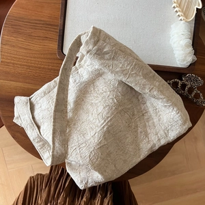 Détail du tissu beige froissé d'un sac cabas minimaliste posé sur une table en bois
