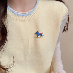 Detail of a rocking horse brooch with blue enamel and crystal inlay on yellow knitwear