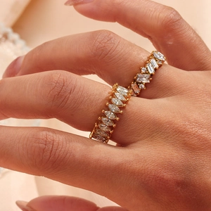 Elegant gold rings set with cubic zirconia stones worn by a model on a beige background