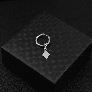 Macro shot of silver diamond-shaped pendant earring on a textured black jewelry box