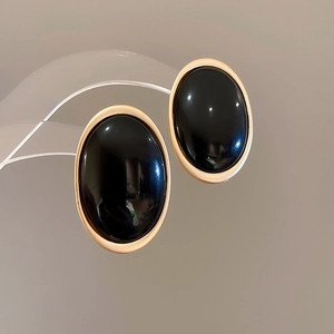 Détail macro de boucles d'oreilles ovales en résine noire avec cadres dorés polis sur support