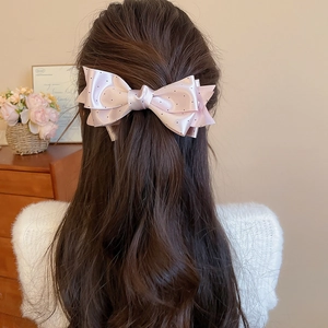 Detail view of a pink polka dot satin bow hair clip styled on wavy brunette hair
