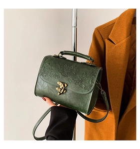 Détail d'un sac bandoulière vert foncé vintage avec motifs floraux gaufrés et fermoir bronze