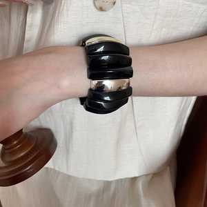 Detail of chunky acrylic and metal segment bracelet worn over a beige linen sleeve