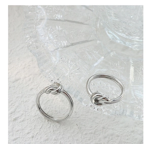 Macro detail of two silver knot rings on a textured white surface with premium glass decor
