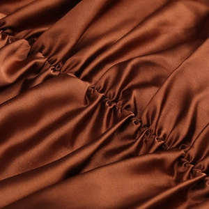 Detailed close-up of dark brown satin fabric with elegant pleated ruffles and silky texture