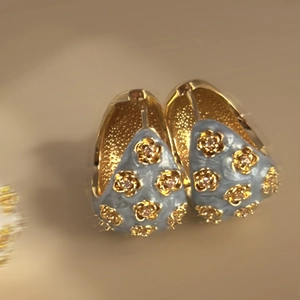 Macro detail of vintage gold C-shape hoop earrings with light blue enamel and floral patterns