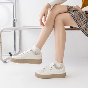 White leather platform sneakers with gum soles and gold basket lettering on feet