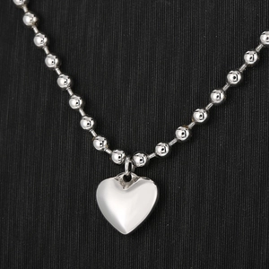 Détail d'un collier de perles argentées avec pendentif cœur sur texture noire
