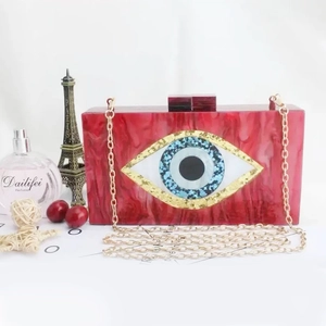 Macro detail of red acrylic evening bag featuring marble texture and devil eye emblem