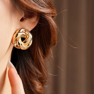 Gros plan sur des boucles d'oreilles nouées dorées portées par un mannequin chic