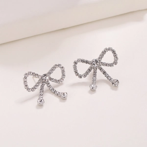 Elegant silver-tone bow earrings with tassels and micro-pave crystals on white stand
