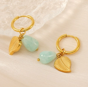 Détail de boucles d'oreilles feuille dorée 18k avec pierres vert clair sur satin