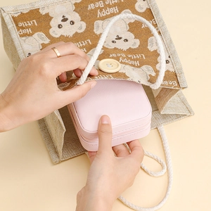 Portable pink faux leather jewelry box with zipper being placed into a small travel bag