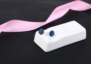 Detail view of round blue crystal stud earrings with glitter on a white ceramic display