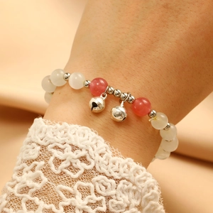 Close-up of beaded bracelet with red and white pearls and silver bells on lace cuff