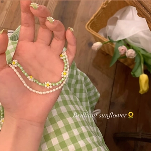 Close-up of layered pearl bracelet set with sunflower pendant and green beaded accents