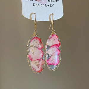 Detalle de pendientes ovalados hechos a mano en oro con resina de flores secas rosas