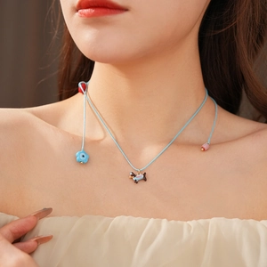 Detail of dachshund puppy pendant and floral beads on blue cord necklace worn by a model