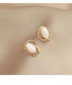 Detailed close-up of golden cat-eye stone earrings with small zircons on beige silk fabric