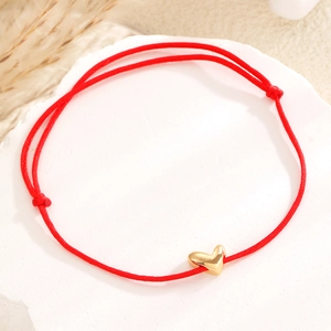 Détail du bracelet en cordon tressé rouge avec pendentif coeur doré sur fond texturé