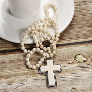 Detail of white marble beaded necklace with silver cross pendant on a coffee cup
