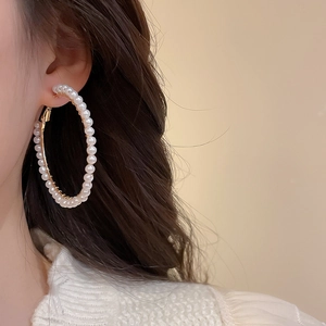 Macro view of large gold hoop earrings with white round pearls on elegant female model