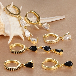Macro view of gold teardrop earrings with white and black zircon on satin fabric