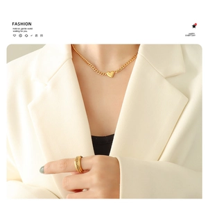 Detail of 18K gold heart pendant necklace and textured ring on elegant white blazer model