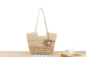 Detail of bohemian straw tote bag featuring hollow weave patterns and floral charm