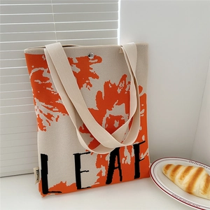 Detail of knitted tote bag with orange leaf pattern and black LEAF lettering on desk