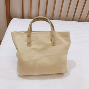 Detail of canvas tote bag showing the tan leather handles and brass rivets