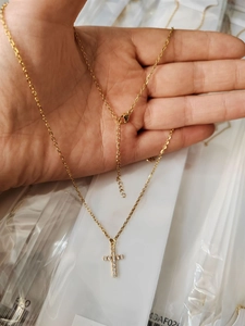 Golden 18K plated cross necklace with mini CZ pavé detail held in hand for scale