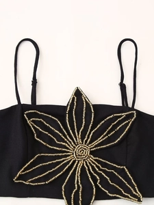 Detail eines schwarzen Crop Tops mit aufwendiger goldener Perlen-Blumenstickerei auf der Brust