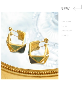 Detail of gold titanium steel earrings with green enamel on a mirror background
