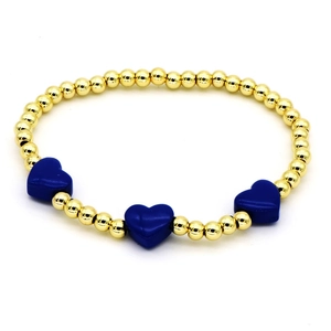 Detailed macro view of golden beaded bracelet with three dark blue enamel heart charms
