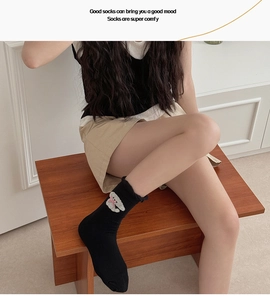 Detail of black knit mid-calf sock with cute bear embroidery and pink bow on model