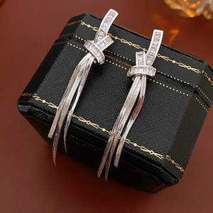 Detailed close-up of zircon knot earrings with silver tassel chains on black jewelry box