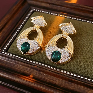 Macro detail of luxury vintage gold earrings with green gemstones in a wooden frame