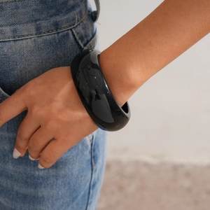 Close-up of a wide glossy black resin bangle on a wrist with minimalist geometric design